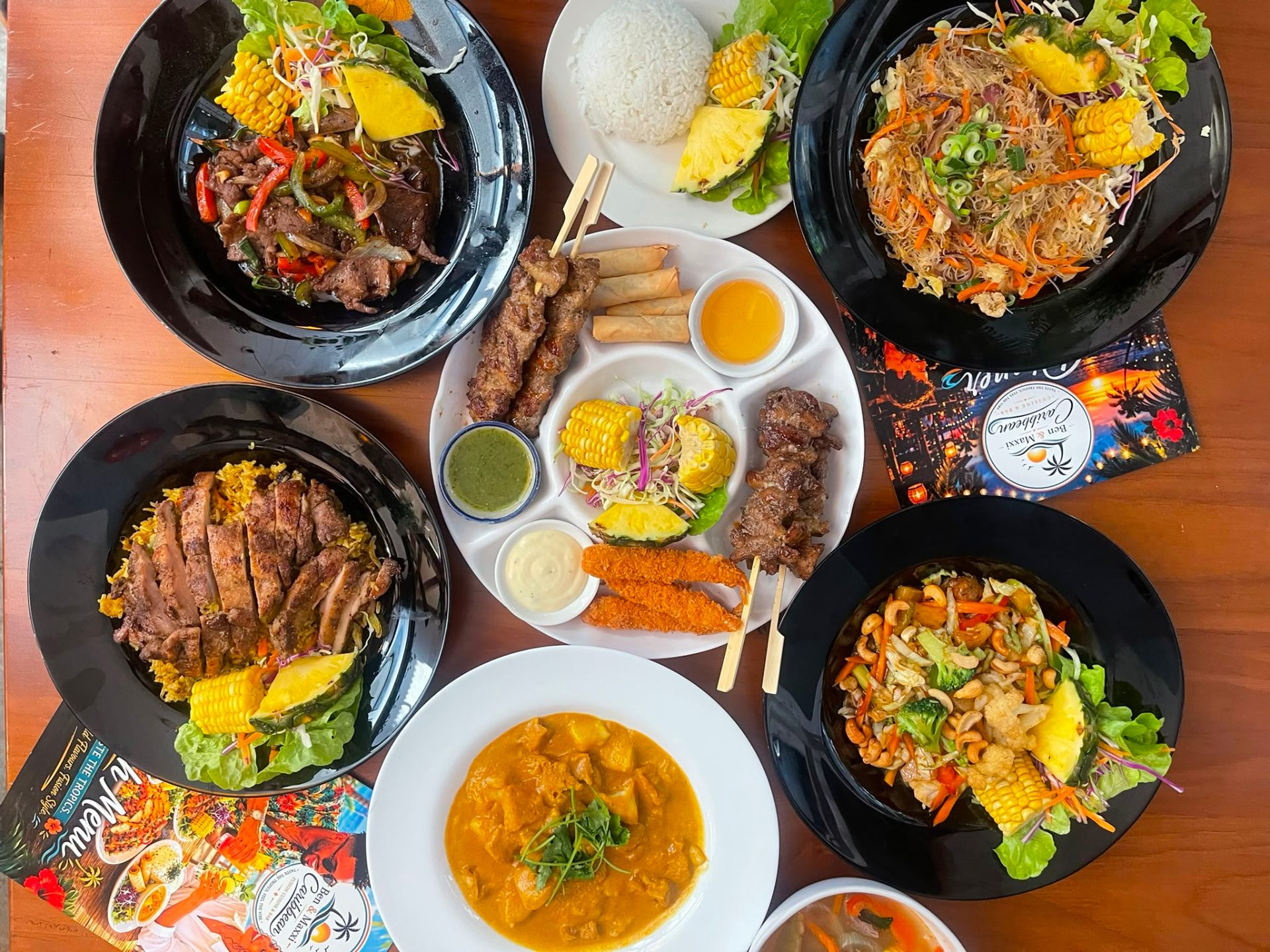 Overhead feast of jerk chicken, curry, noodles and skewers